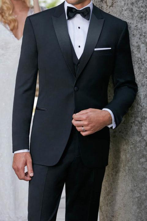 Man wearing a black tuxedo with a bow tie against a neutral background